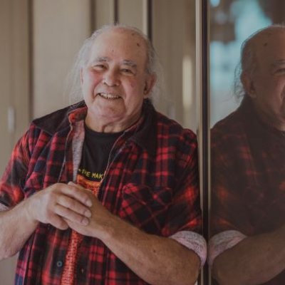 a man in a check shirt leans against a window in which he is reflected